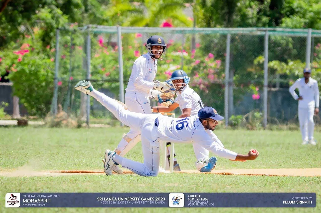 Muftee diving full stretch at short leg with the ball in his outstretched hand, the batter turning to watch
