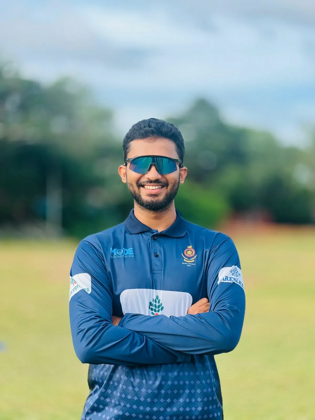 Muftee in University of Moratuwa cricket kit, arms folded, standing on the outfield