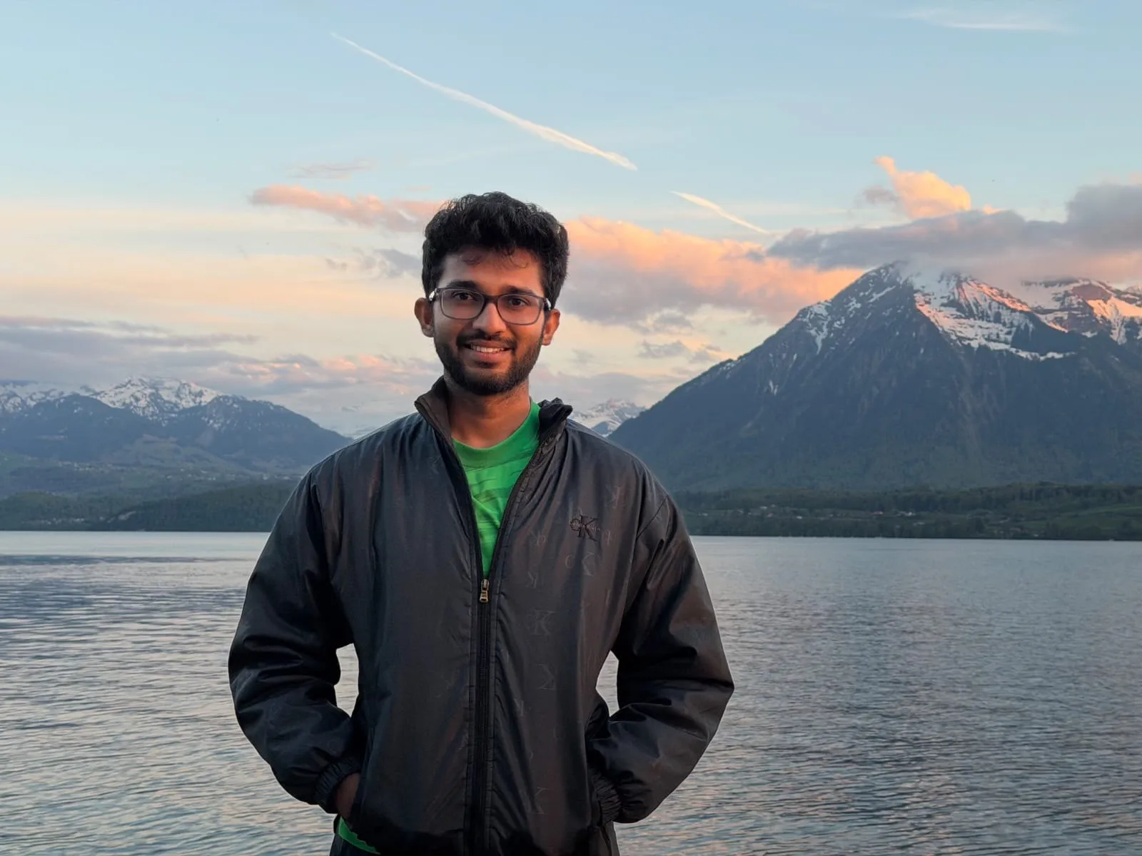 Muftee at the edge of a lake at dusk, snow-capped peaks catching the last light behind him